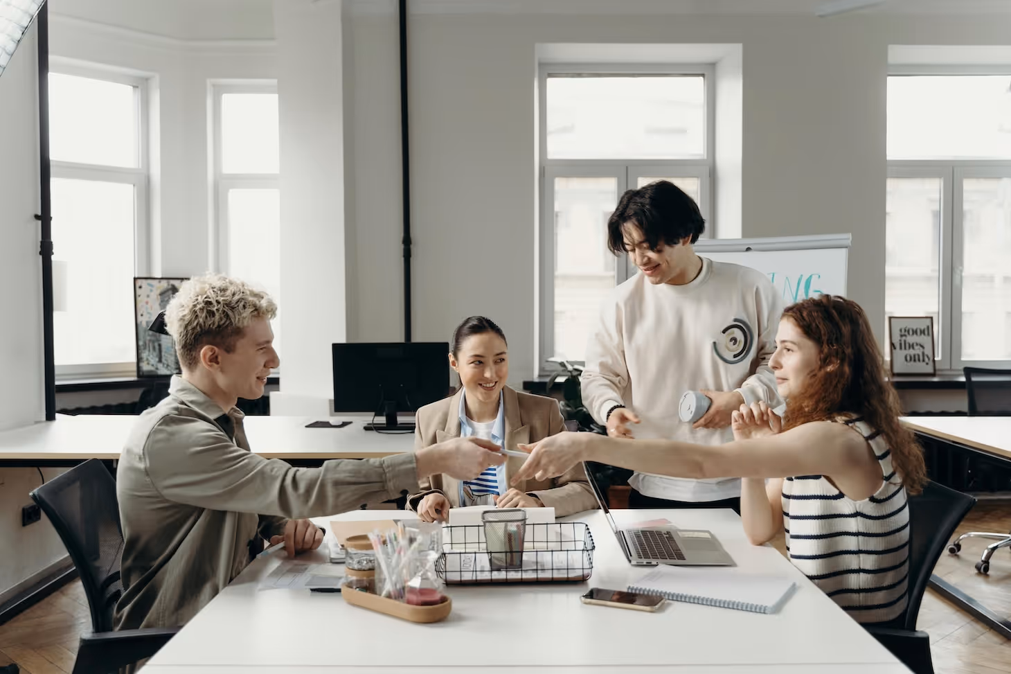 Vier junge Erwachsene arbeiten gemeinsam in einem modernen Büro, lachen und tauschen Papiere aus.